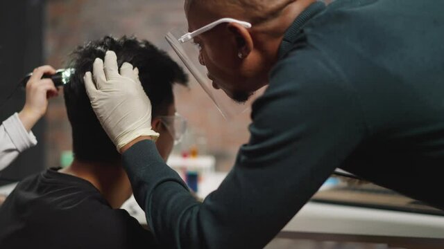 African-American biologist examines man hair and head skin while little girl use scanner in laboratory close backside view