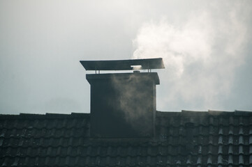 Ein rauchender Schornstein auf einem schwarz gedeckten Spitzdach