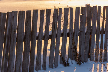 Old fence in the village at sunrise in winter.