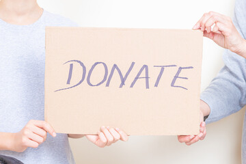 Donation, charity concept. Kid and woman hands holding brown piece of cardboard with inscription Donate. Close up