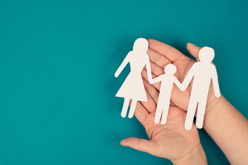 Parents with one child holding hands, paper cut out, copy space, petrol colored background,...