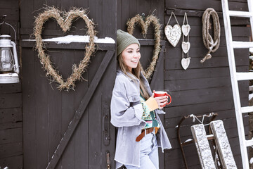young asian woman holds cup of mulled wine in hands in courtyard of suburban house in winter, concept of Christmas and New Year vacation on farm, family love and support