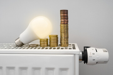 Energy crisis. White LED light bulb on a radiator with money coin stack. Growing electric and gas...