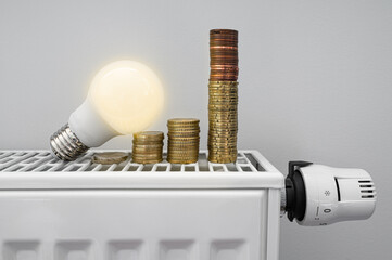 Energy crisis. White LED light bulb on a radiator with money coin stack. Growing electric and gas...