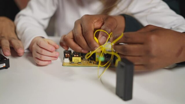 African-American man technician teaches little girl student to connect wires with probes to chip at table in science laboratory close view