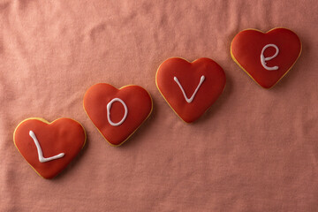 The word "love" laid out from bottom to top on red gingerbread in the shape of a heart. Valentine's day concept. The word love on a pink background.