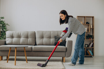 Woman doing house work with rechargeable vacuum cleaner - obrazy, fototapety, plakaty