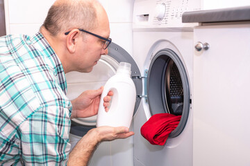 Mazhchina Caucasian washes clothes in a washing machine and uses household chemicals. Household chores.