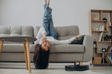 Woman using phone while robot vacuum cleaner cleaning up the room