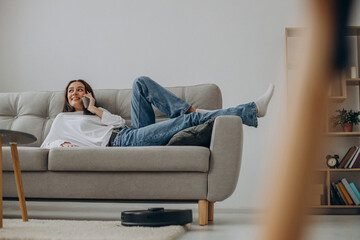 Woman using phone while robot vacuum cleaner cleaning up the room