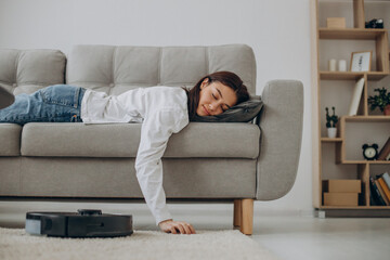 Woman sleeping on sofa while robot vacuum cleaner cleaning up the room