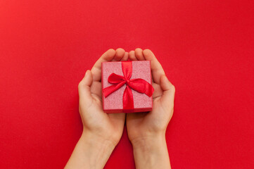 a red gift box in the hands of a child on a red background