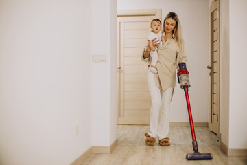 Mother vacuuming with baby daughter at home with the help of rechargeable vacuum cleaner