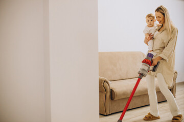 Mother vacuuming with baby daughter at home with the help of rechargeable vacuum cleaner