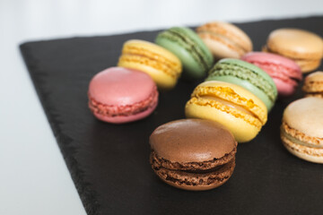 Colorful macaroons on a black slate stone served on a white table, Delicious French almond cookies, dessert.