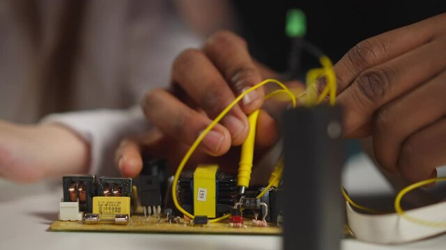 African-American technician touches diodes on chip with probes doing experiment to explain to little student at table in science laboratory closeup