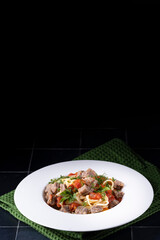 Pasta in tomato sauce and meat on white plate and black ceramic background