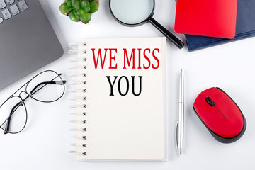 WE MISS YOU text on a notepad with laptop on the white background