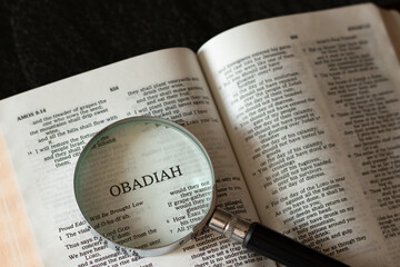 Obadiah prophet open Holy Bible Book with a magnifying glass on dark granite background. Searching...