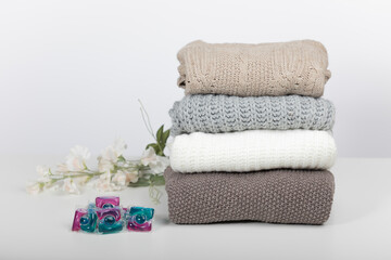 wool sweaters folded on a white table and white background with a decorative flower and washing machine pads