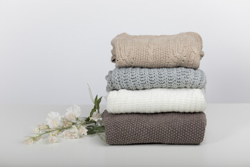wool sweaters folded on a table and a white background with a decorative flower
