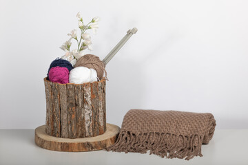 wooden basket with balls of wool and knitting needles together with a handmade scarf on white background