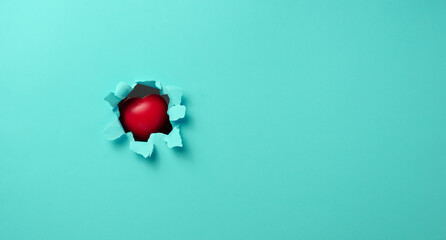 red heart sticks out in a hole with torn edges in blue paper