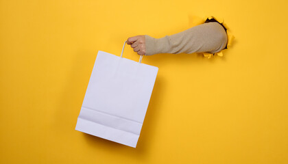 female hand holds a white paper disposable bag with handles for groceries and clothes. Recyclable...
