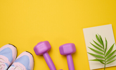 pair of pink sneakers and purple dumbbells on a yellow background, sports. Copy space