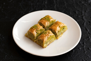 Pistachio baklava dessert on a dark background. Turkish sweet dessert concept. plate of pistachio baklava. sherbet sweet Mediterranean bakery. close up. selective focus.