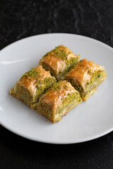 Pistachio baklava dessert on a dark background. Turkish sweet dessert concept. plate of pistachio baklava. sherbet sweet Mediterranean bakery. close up. selective focus.