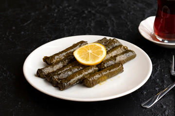 Delicious dolma (sarma) stuffed grape leaves rice, white yogurt sauce. Stuffed grape leaves on dark background. Lebanese dolma sarma on plate. Lebanon turkish greek middle eastern cuisine.