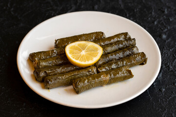 Delicious dolma (sarma) stuffed grape leaves rice, white yogurt sauce. Stuffed grape leaves on dark background. Lebanese dolma sarma on plate. Lebanon turkish greek middle eastern cuisine.