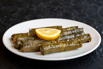 Delicious dolma (sarma) stuffed grape leaves rice, white yogurt sauce. Stuffed grape leaves on dark background. Lebanese dolma sarma on plate. Lebanon turkish greek middle eastern cuisine.