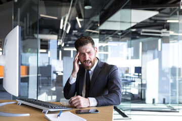Businessman working in the office at a desk with a computer, a tired man has a severe headache