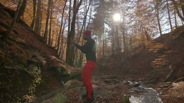Young adult standing on a rock near stream in autumn forest, turns to take a photo. Lens flare