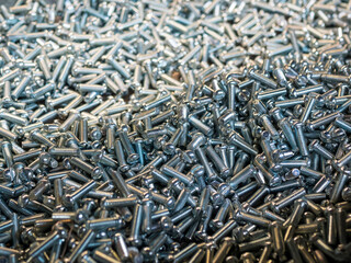 Background of shiny metallic screws, selective focus. Plenty of metal pins with a spiral ridge along the length