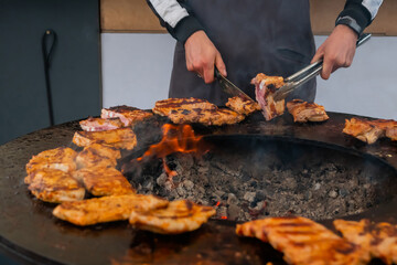Chef holding knife, cutting fresh juicy meat steaks on brazier at summer local food market - close up view. Outdoor cooking, gastronomy, cookery, street food concept