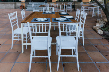 Fototapeta na wymiar Front image of a wooden terrace table with 8 white chairs around it ready to eat.