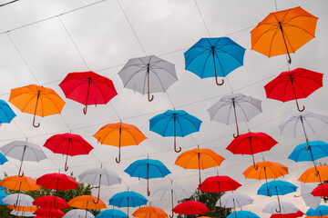 Fototapeta na wymiar Colorful umbrellas hanging against gray overcast sky and swaying in wind at summer city festival - low angle view. Street decoration, celebration, art, holiday concept