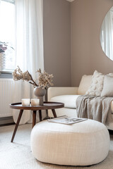 Scandinavian living room interior. Round table with candles and vase. A sofa with cosy blankets.