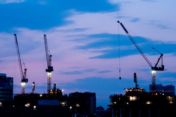 Tower cranes silhouettes and unfinished building construction against night sky. Evening time, low light. Building process, construction, engineering, industrial and development concept