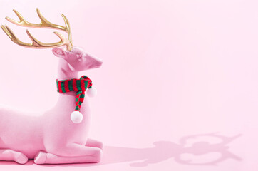 A pink reindeer with golden horns and a striped red and green scarf on pastel pink background. Minimal winter  season creative concept for web banner or card. Surreal Christmas or New Year design © Miss V