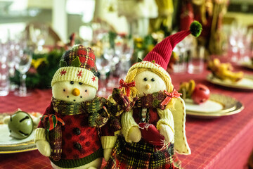 Wonderful table for the celebration of Christmas set up with plates, glasses, wine glasses, and golden cutlery with ornaments in red tones. Christmas ornaments on the table.
