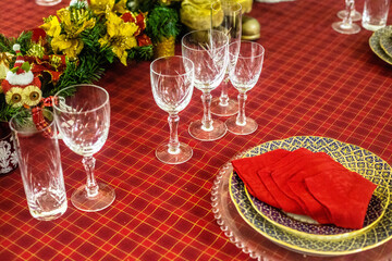 Wonderful table for the celebration of Christmas set up with plates, glasses, wine glasses, and golden cutlery with ornaments in red tones. Christmas ornaments on the table.