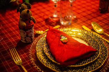 Wonderful table for the celebration of Christmas set up with plates, glasses, wine glasses, and golden cutlery with ornaments in red tones. Christmas ornaments on the table.
