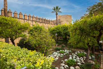 Fototapeta premium Gardens at the Alcazar de los Reyes Cristianos in Cordoba, Spain. Part of a stone wall and a tower surrounded by fruit trees and flowers
