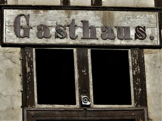 Altes hölzernes Gasthaus-Schild über leeren Fensterhöhlen