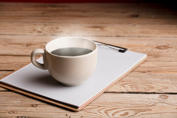 cup of coffee, tea or chocolate, soft beige color with hot steam and notebook on rustic wooden table