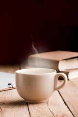 off white cup with chocolate, tea or coffee, hot steam, books on rustic wooden table with red background